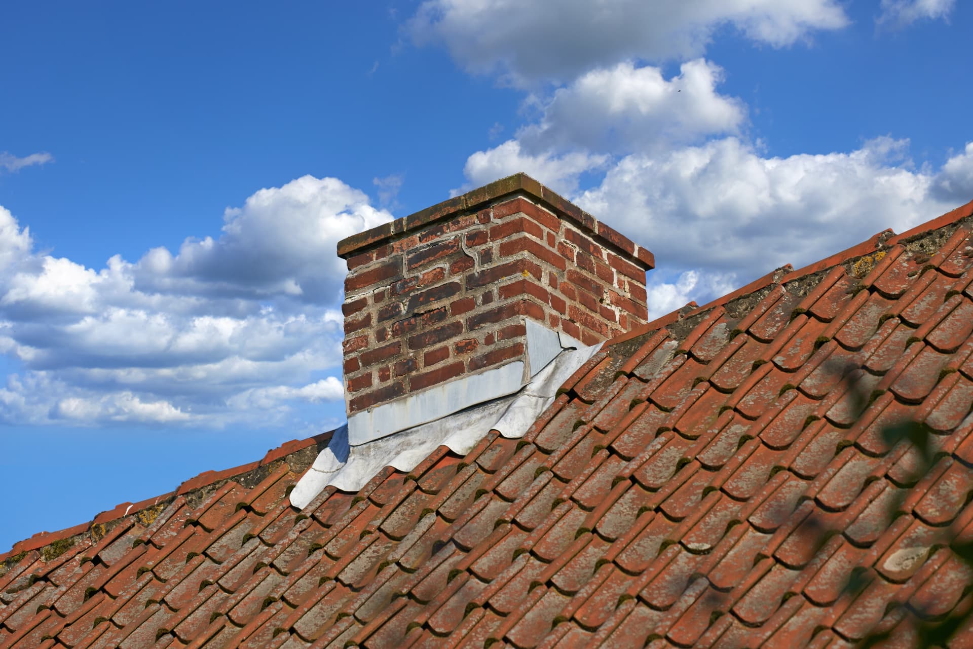 Brick chimney stack with cracked mortar joints and lead flashing on a red tiled roof