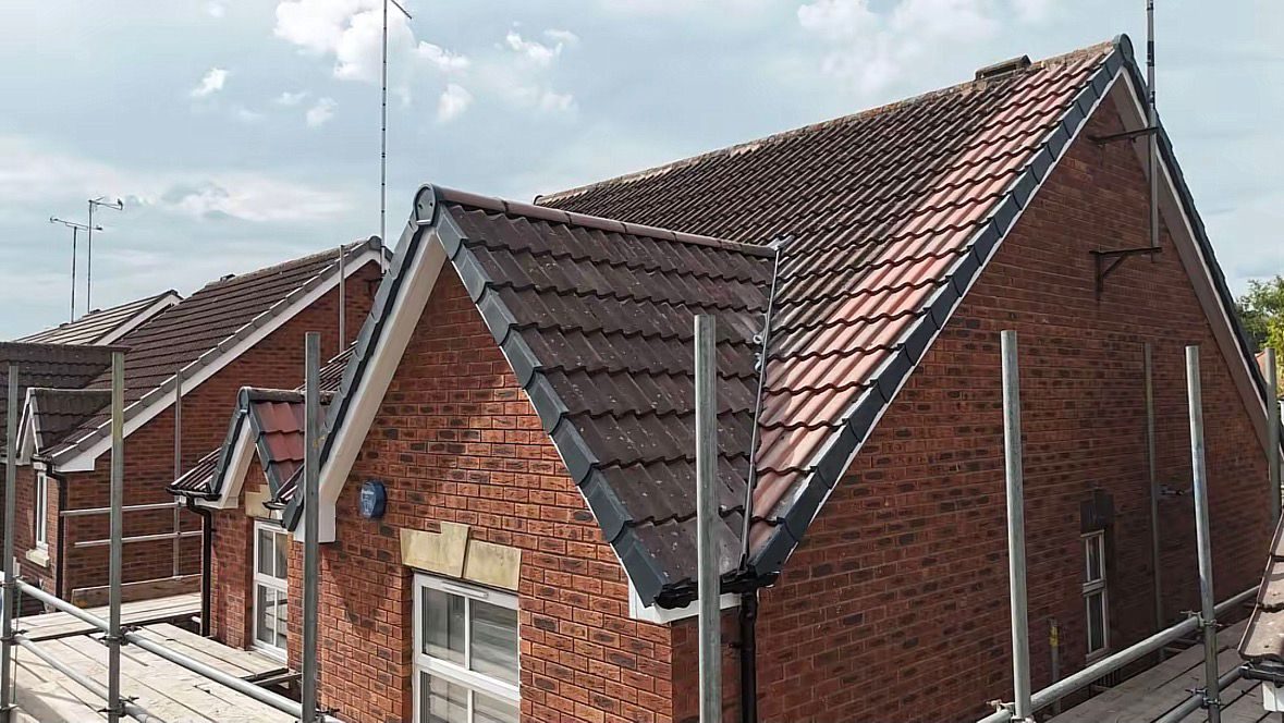 Newly tiled pitched roof with dry verge trims on a brick house under scaffold